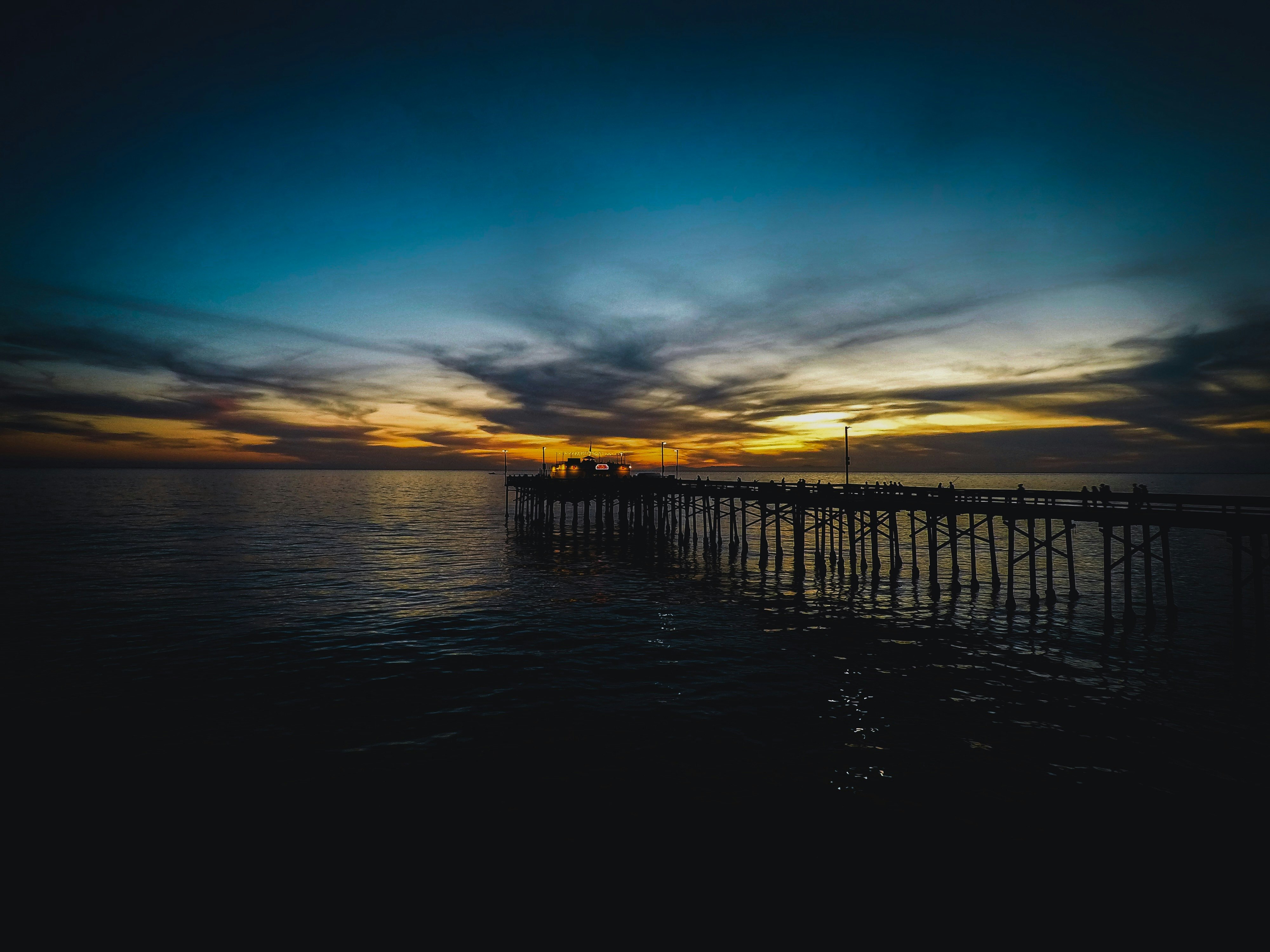 silhouette of dock on body of water during sunset